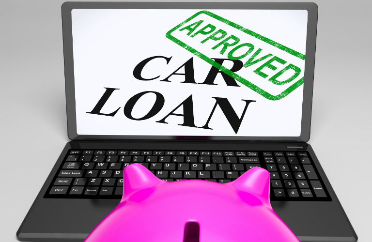 A Piggy bank looking at a computer screen that has text showing car loan approved